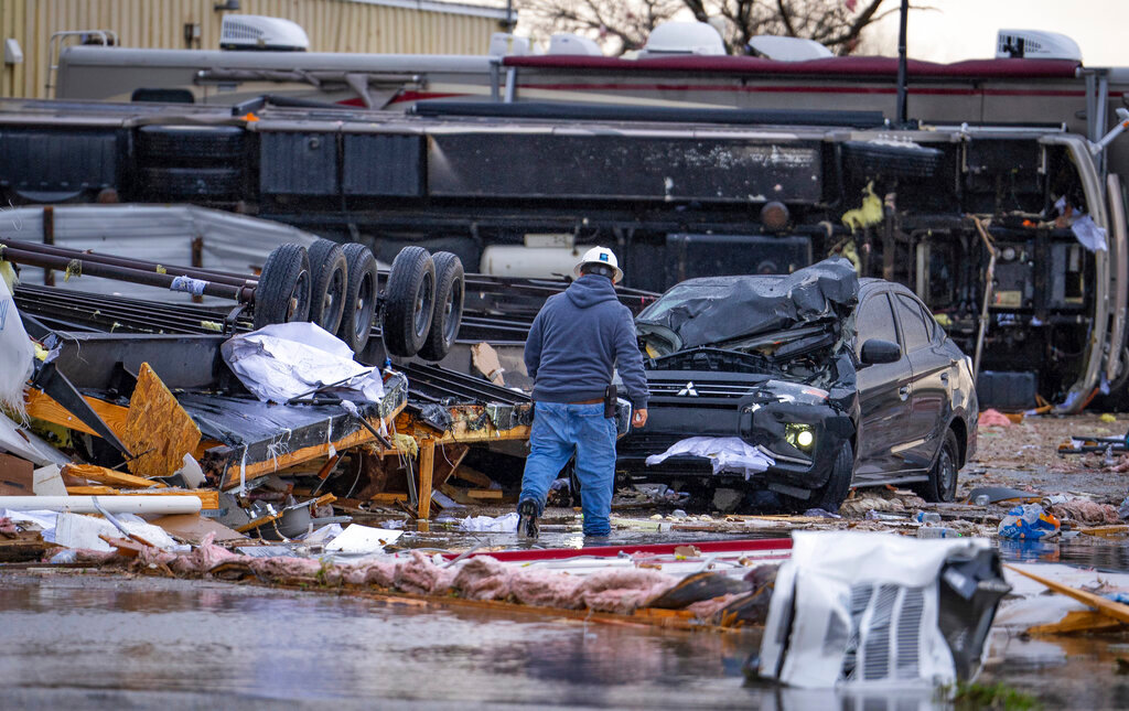 A man walks through a parking lot containing multiple overturned vehicles, including a trailer that was in a parking lot across the street, according to people at the scene, where a tornado was reported Tuesday, Jan. 24, 2023, in Pasadena, Texas. (Mark Mulligan/Houston Chronicle via AP)