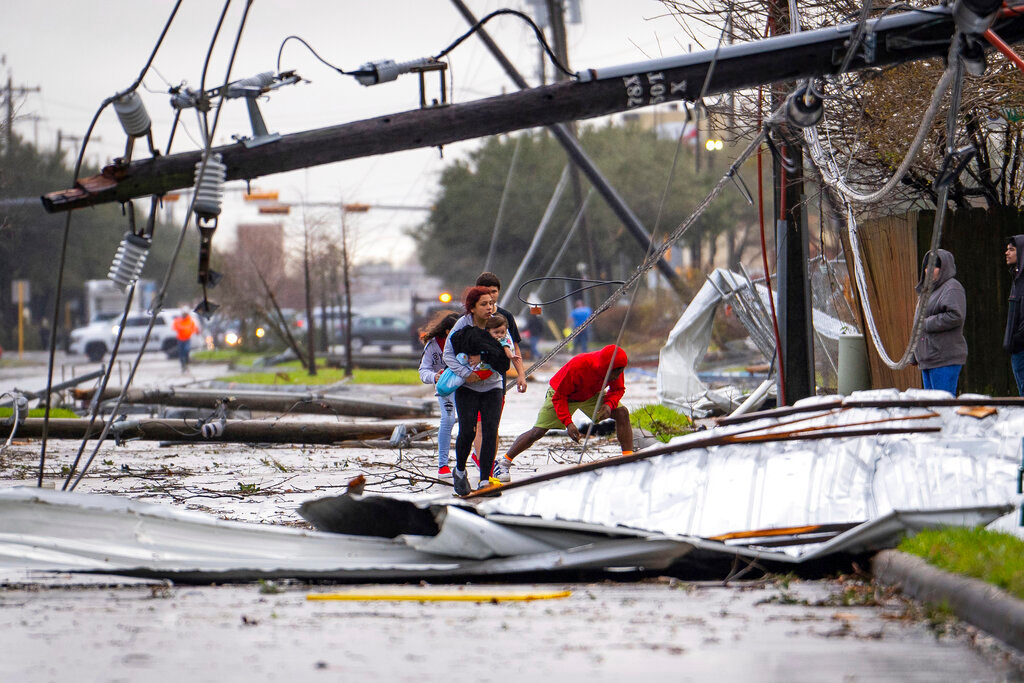 People cross under downed power lines where a tornado was reported Tuesday, Jan. 24, 2023, in Pasadena, Texas. (Mark Mulligan/Houston Chronicle via AP)