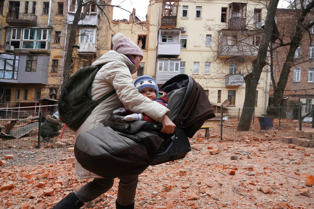 A woman carries her child as they evacuate from a residential building which was hit by a Russian rocket at the city center of Kharkiv, Ukraine, Monday, Jan. 30, 2023. (AP Photo/Andrii Marienko)