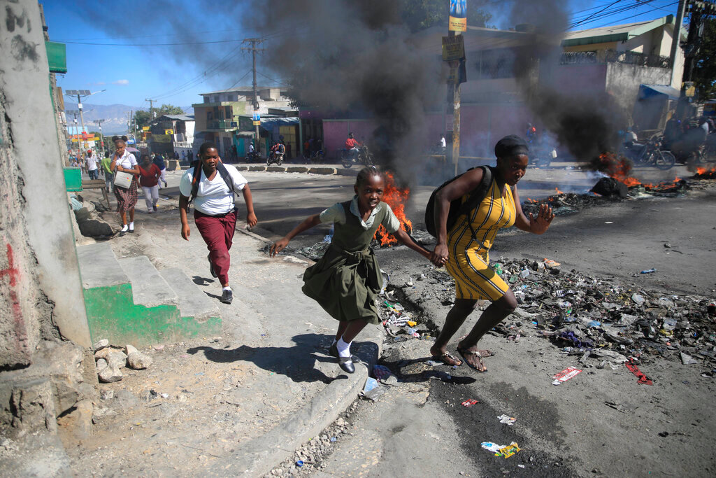 A woman and her daughter run past a barricade that was set up by police protesting bad police governance in Port-au-Prince, Haiti, Jan. 26, 2023. (AP Photo/Odelyn Joseph, File)