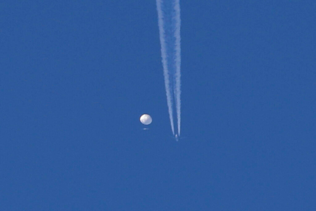 In this photo provided by Brian Branch, a large balloon drifts above the Kingstown, N.C. area, with an airplane and its contrail seen below it. The United States says it is a Chinese spy balloon moving east over America at an altitude of about 60,000 feet (18,600 meters), but China insists the balloon is just an errant civilian airship used mainly for meteorological research that went off course due to winds and has only limited “self-steering” capabilities. (Brian Branch via AP)