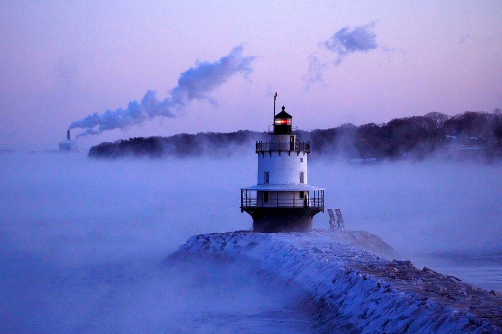 Spring Point Ledge Light is surrounded by arctic sea smoke while emissions from the Wyman Power plant, background, are blown horizontal by the fierce wind, Saturday, Feb. 4, 2023, in South Portland, Maine. The morning temperature was about -10 degrees Fahrenheit. (AP Photo/Robert F. Bukaty)