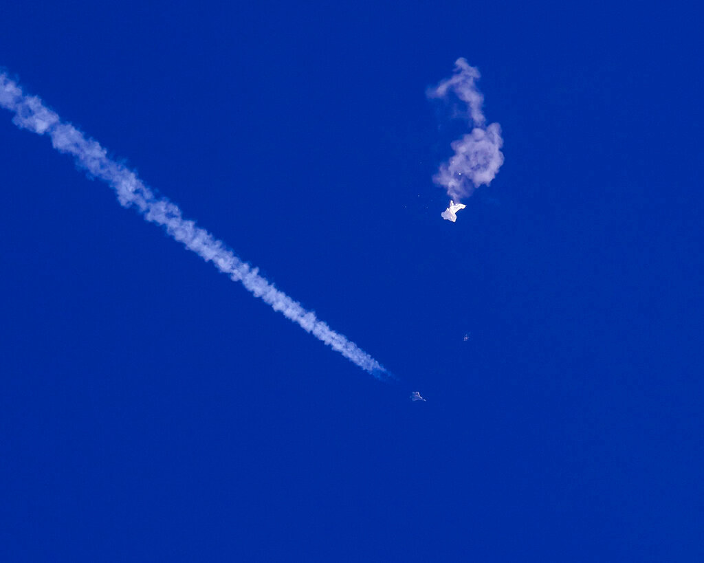 The remnants of a large balloon drift above the Atlantic Ocean, just off the coast of South Carolina, with a fighter jet and its contrail seen below it, Saturday, Feb. 4, 2023. (Chad Fish via AP)
