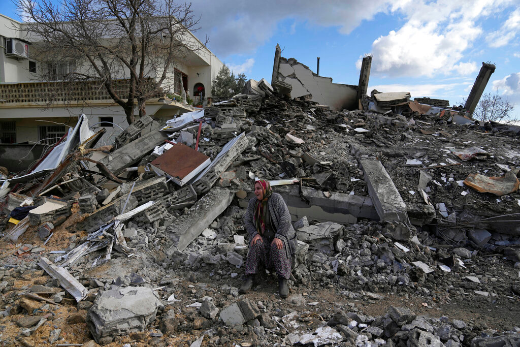 A woman sits on the rubble as emergency rescue teams search for people under the remains of destroyed buildings in the town of Nurdagi on the outskirts of Osmaniy, southern Turkey, Tuesday, Feb. 7, 2023. (AP Photo/Khalil Hamra)