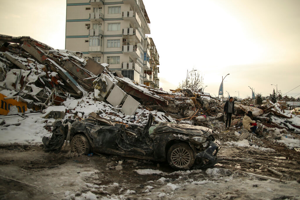 People sit by a collapsed building in Malatya, Turkey, Tuesday, Feb. 7, 2023. (AP Photo/Emrah Gurel)