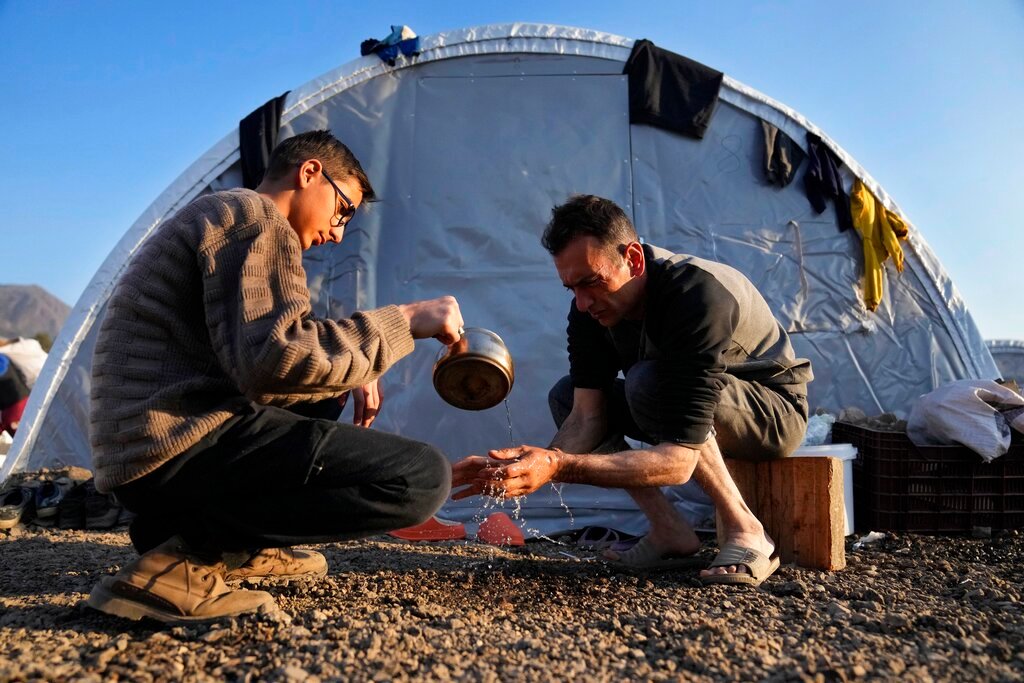 A boy helps his father wash his hands at a makeshift camp where they settled after losing their house in a devastating earthquake, in Iskenderun, southern Turkey, on Feb. 14, 2023. (AP Photo/Hussein Malla)