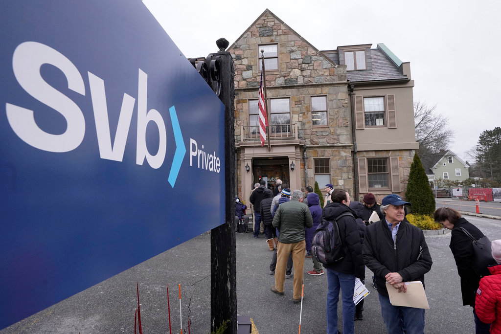 Customers and bystanders form a line outside a Silicon Valley Bank branch location, Monday, March 13, 2023, in Wellesley, Mass. (AP Photo/Steven Senne, File)
