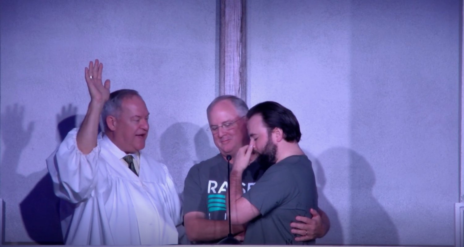 Davy Register, center, prepares to baptize his son, Dalton, while Pastor Robby Foster raises his hand in celebration of the event.