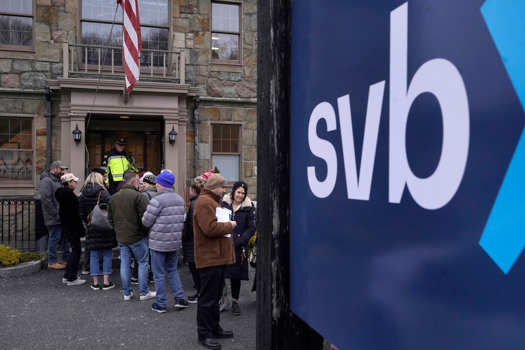 A law enforcement official, behind, stands in an entryway to a Silicon Valley Bank branch location, March 13, 2023, as customers and bystanders line up outside the bank, in Wellesley, Mass. A new poll finds that only 10% of U.S. adults say they have high confidence in the nation’s banks and other financial institutions. That's down from the 22% who said they had high confidence in banks in 2020. Following the collapse of Silicon Valley Bank this month, the poll from The Associated Press-NORC Center for Public Affairs Research also finds that a majority say the government is not doing enough to regulate the industry. (AP Photo/Steven Senne, File)