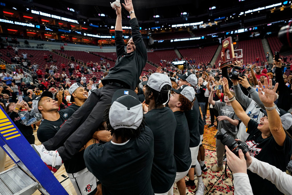 San Diego State head coach Brian Dutcher holds the remains of the net and is falls into the arms of his team after they defeated Creighton in an Elite 8 game in the South Regional of the NCAA Tournament, Sunday, March 26, 2023, in Louisville, Ky. San Diego State won 57-56. (AP Photo/Mike Stewart)