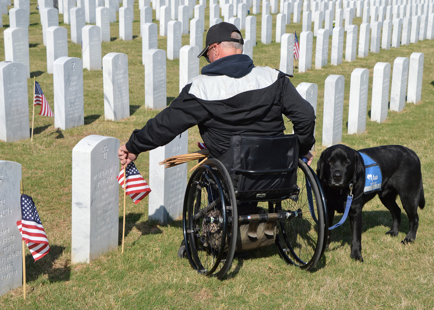 Don Dowling, accmpanied by his dog Coop, places a flag on a grave at the Georgia National Cemetery in Canton, Ga., Saturday, May 27, 2023. (Index/Henry Durand)