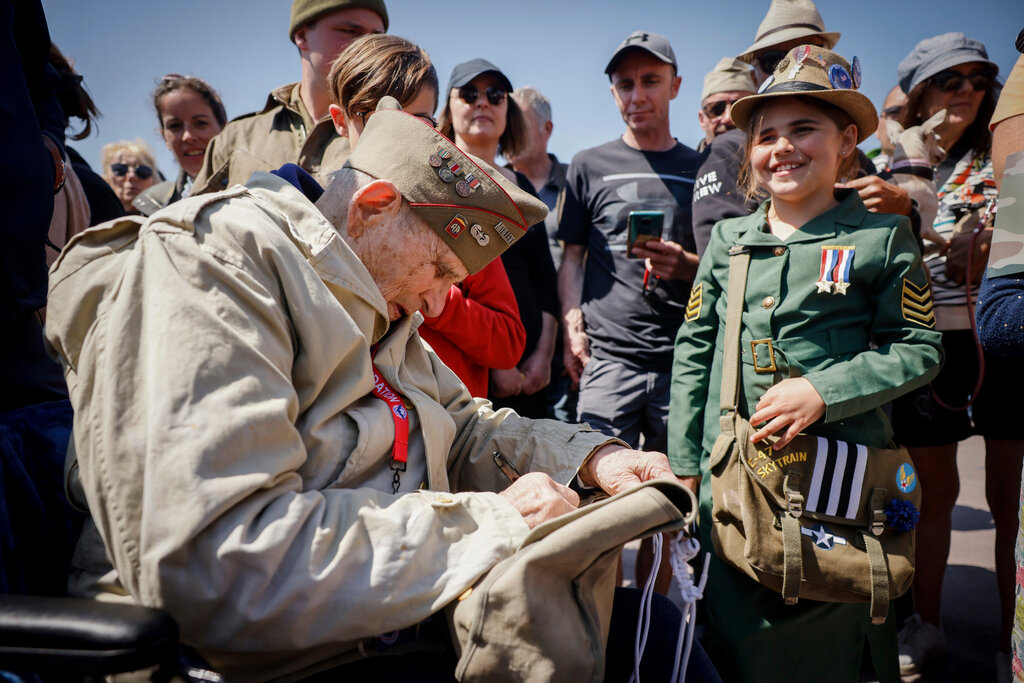 A U.S. veteran signs the bag of a World War II enthusiast during a gathering in preparation of the 79th D-Day anniversary in Sainte-Mere-Eglise Normandy, France, Sunday, June 4, 2023. (AP Photo/Thomas Padilla)