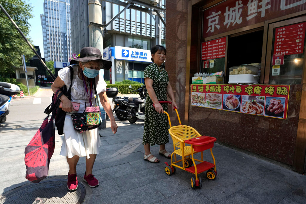 An elderly woman walks by a store selling snacks in Beijing, Monday, July 17, 2023. (AP Photo/Ng Han Guan)