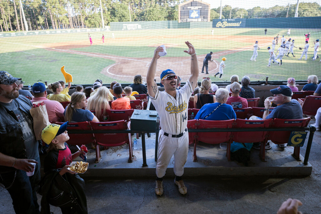 Savannah Bananas catcher Vinny Rauso, center, tries to get fans to cheer before throwing a free T-shirt to the loudest section, during the team's game against the Florence Flamingos, June 7, 2022, in Savannah, Ga. (AP Photo/Stephen B. Morton, File)