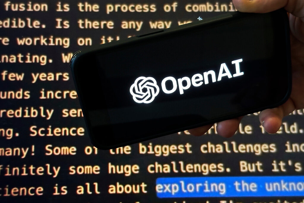 The OpenAI logo appears on a mobile phone in front of a screen showing part of the company website in this photo taken on Nov. 21, 2023, in New York. (AP Photo/Peter Morgan, File)