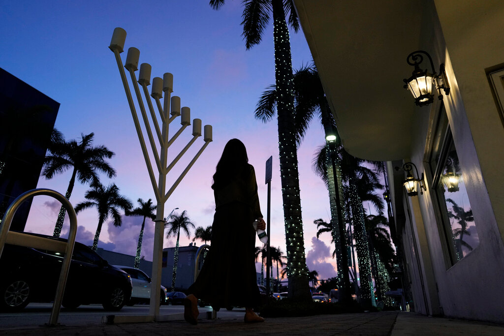 A woman in conservative dress walks past a menorah standing outside a Jewish synagogue ahead of the start of Hanukkah, in Miami Beach, Fla., Friday, Dec. 1, 2023. (AP Photo/Rebecca Blackwell)