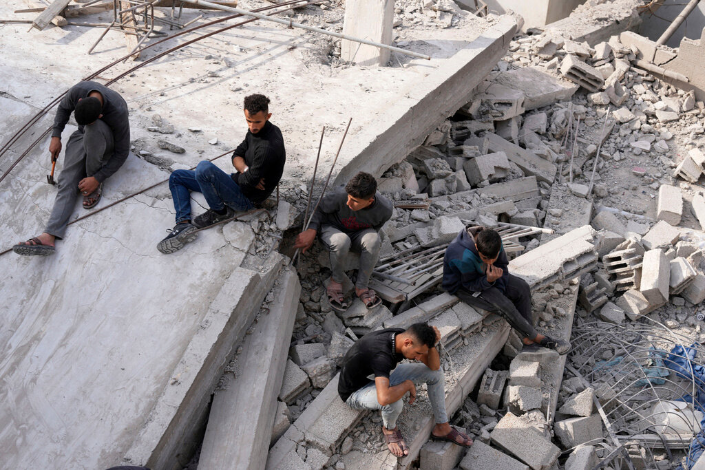 Palestinians sit by the building of the Al-Nadi family destroyed in the Israeli bombardment of the Gaza Strip in Nusseirat refugee camp, central Gaza Strip, early Friday, Dec. 8, 2023. (AP Photo/Adel Hana)