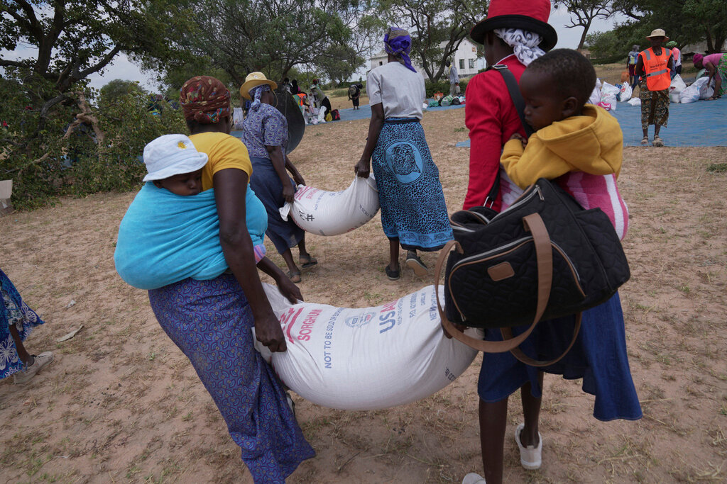 Zanyiwe Ncube, left, carries a bag of sorghum during a food distribution in Mangwe district in southwestern Zimbabwe, March, 22, 2024. (AP Photo/Tsvangirayi Mukwazhi, File)