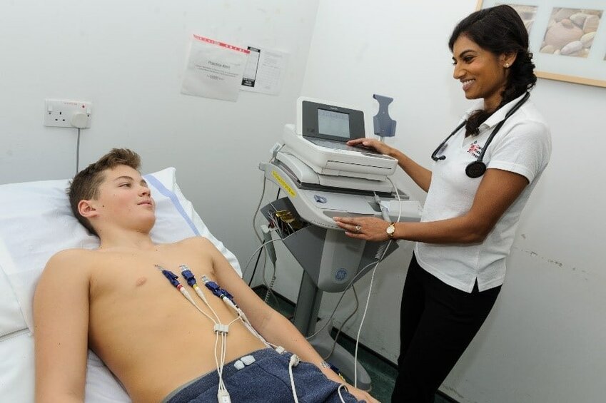 A boy receives a preventative health screening with an electrocardiogram fixed to his chest.