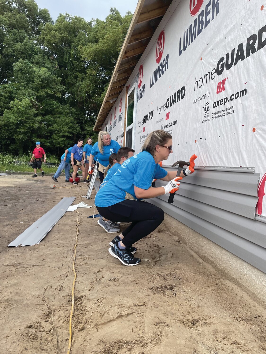 Volunteers cut and plaster vinyl panels to line the perimeter of two new houses being built in Green Cove Springs.