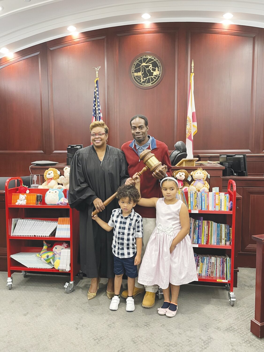 Cox and the Sweeting family – Clint (behind), Donovan (front), Kalina (right) – pose with a ceremonial gavel in the courtroom. Afterward, Donovan and Kalina were invited to a book and stuffed animal, too.