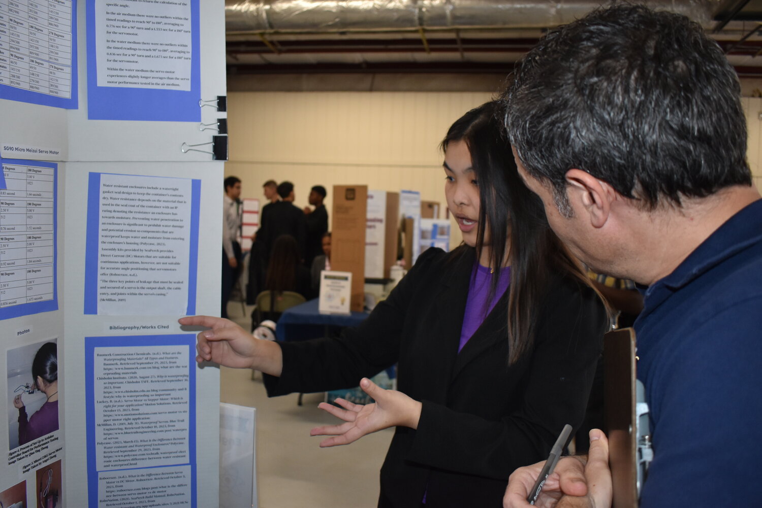 Judge and engineer Ray Morin listened to Angel Zheng explain the hypothesis, examination, and conclusion of her project on the waterproofing and experimentation of servo motors.
