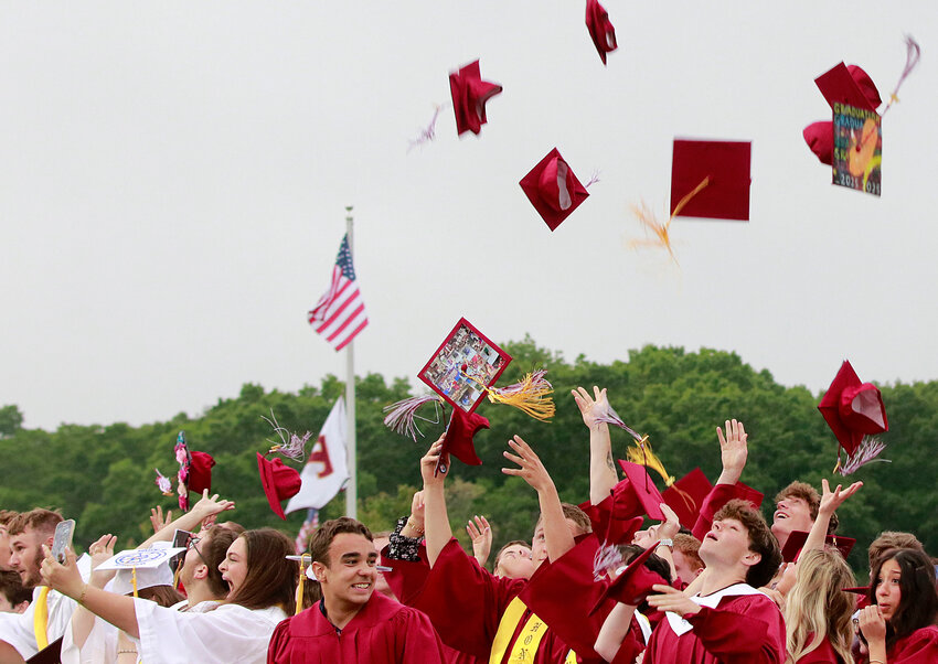 Seth Aguiar (left) and the class hoist their hats into the air after commencement.