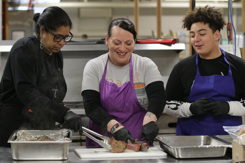 Roxanne DeBrito (left), Erica Harris and son, Jerome Harris prepare a corned beef and cabbage meal for clients at the Good Neighbors food kitchen on Monday. 