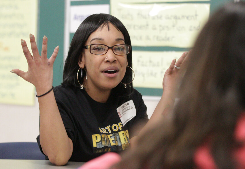 Author Sarah Ashley discusses writing techniques with eighth-grade students gathered around a table.