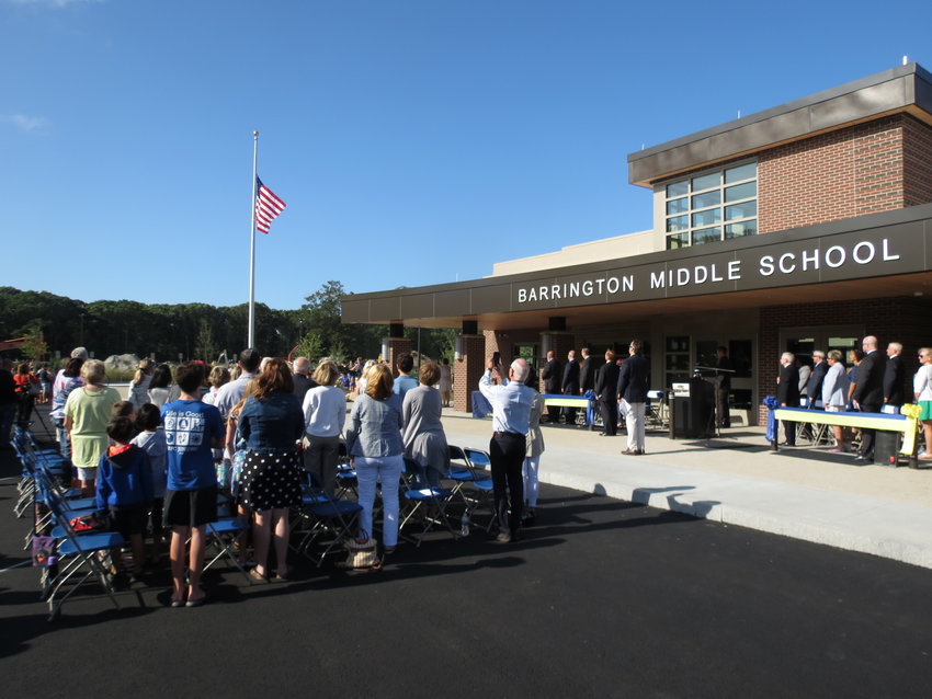 People stand during the playing of the National Anthem and raising of the flag in front of the new Barrington Middle School during a special grand opening ceremony in 2019. Officials recently announced the project will have a $4.3 million surplus.