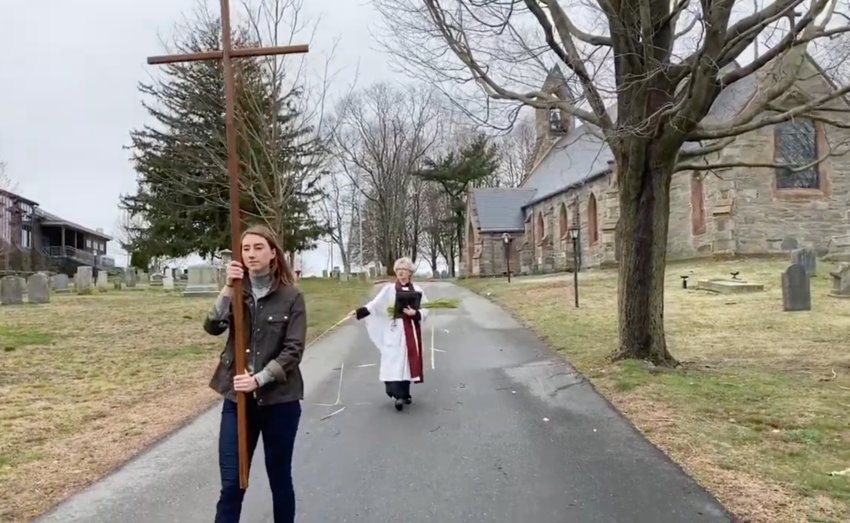 In a video still from an online Palm Sunday service, Lydia DeAngelo leads a brief processional from the chapel to the home of her mother, Jennifer Pedrick (read), rector of St. Mary&rsquo;s Episcopal Church.