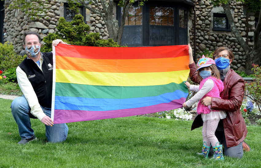 Barrington Town Council member Jacob Brier (left) holds a Pride flag with Sara Jordeno (right) and her daughter Isra Ruf, 3, in front of the town hall. A flag-raising event is planned at the town hall for June 15.