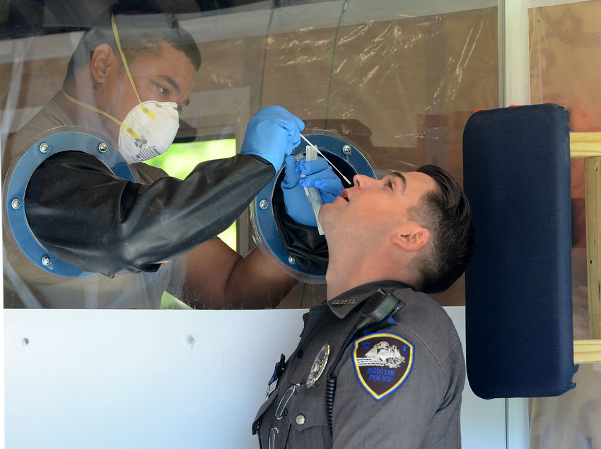 Bristol Patrolman Sean Gonsalves is about to have the COVID-19 test administered by a member of the Rhode Island National Guard, who operates behind a protective shield inside a mobile trailer.