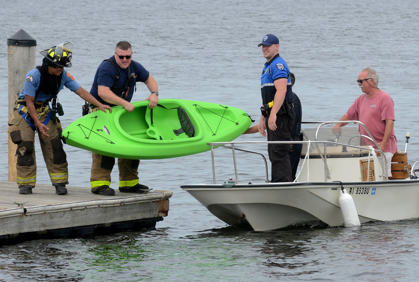 A police officer hands a firefighter the kayak that took on water and sank in Hundred Acre Cove on Thursday, May 28.