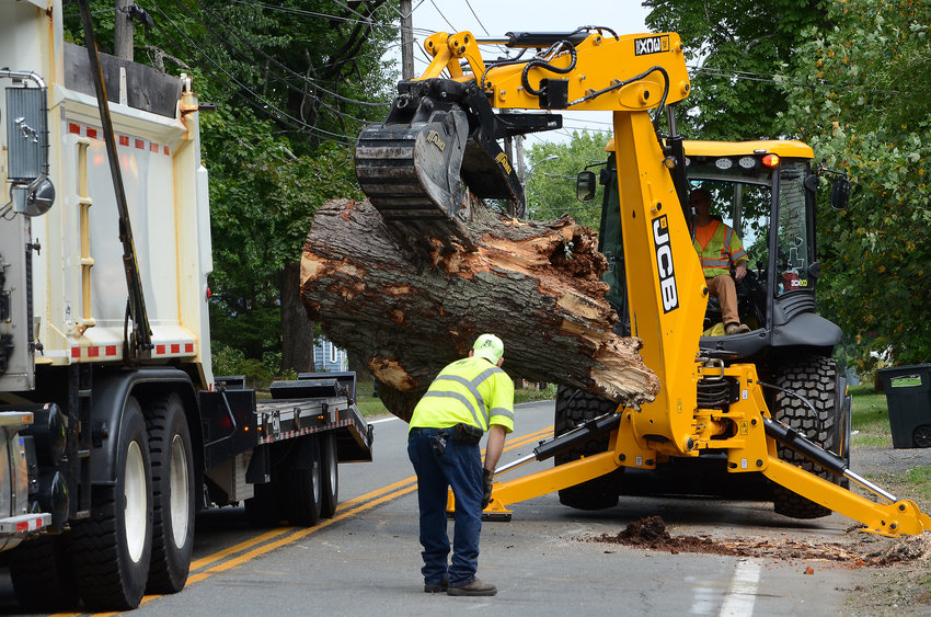 Crews from the Barrington Department of Public Works, RI DOT, and various tree contractors were busy cleaning up after a fast-moving storm swept through Barrington on Tuesday, Aug. 4. The storm knocked out power to thousands of residents and blocked roadways with downed trees and limbs. Pictured, Rhode Island Department of Transportation backhoe operator Tony Calci and his assistant lift a large section of fallen tree that had been blocking Sowams Road.