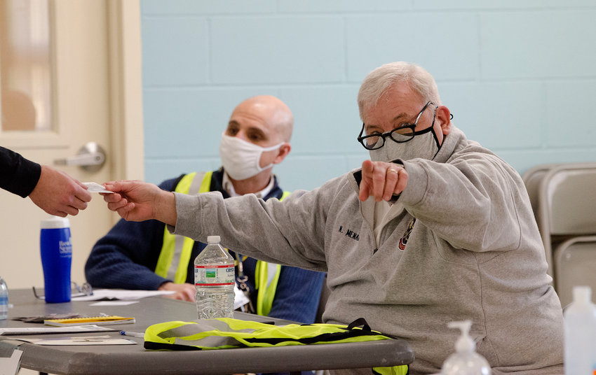 Norm Menard, of Barrington EMS, gives instruction while checking someone in at Quinta Gamelin Recreation Center, where health workers and first responders can get the COVID-19 vaccine.