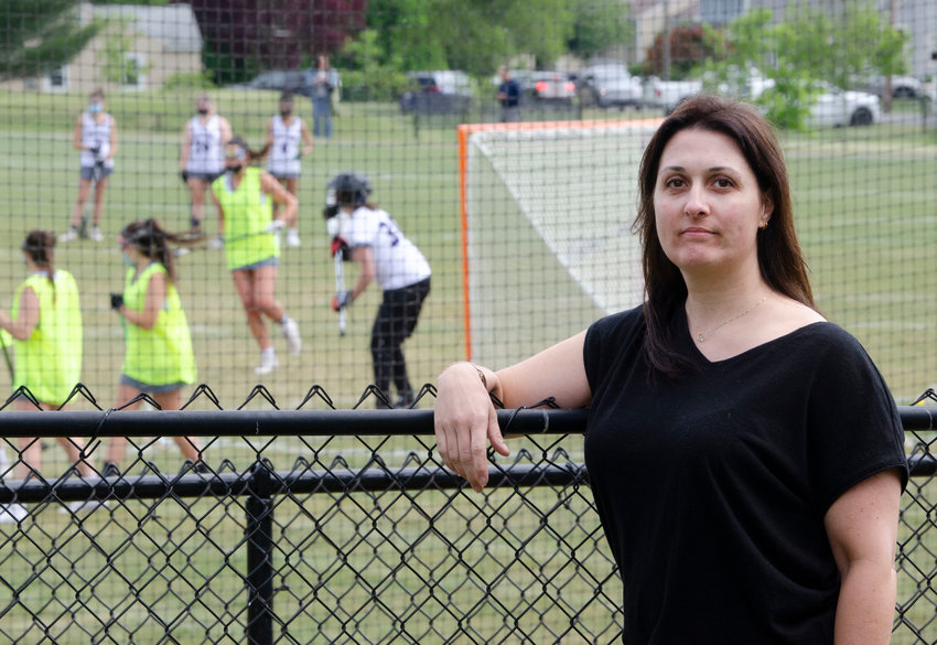 Susan Pasqual leans against her back fence, with the warmup for a Mt. Hope girls&rsquo; lacrosse game taking place in the background.