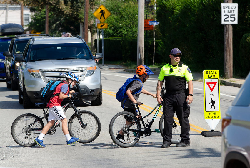 Barrington patrolman Tim Oser helps Hampden Meadow's students and their parents cross County Road to avoid road work on Wednesday.
