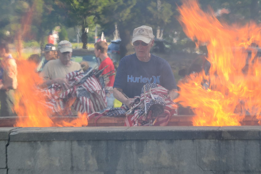 Ed Little, cloaked in smoke and surrounded by flames, prepares to throw a batch of retired American flags into the burn pit at the Pete Sepe Pavilion on Monday evening.