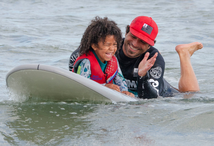 Gnome Surf Therapy founder Chris Antao works with Nora Senghore, 6, as she learns to surf at South Shore Beach in Little Compton one recent Saturday.&nbsp;
