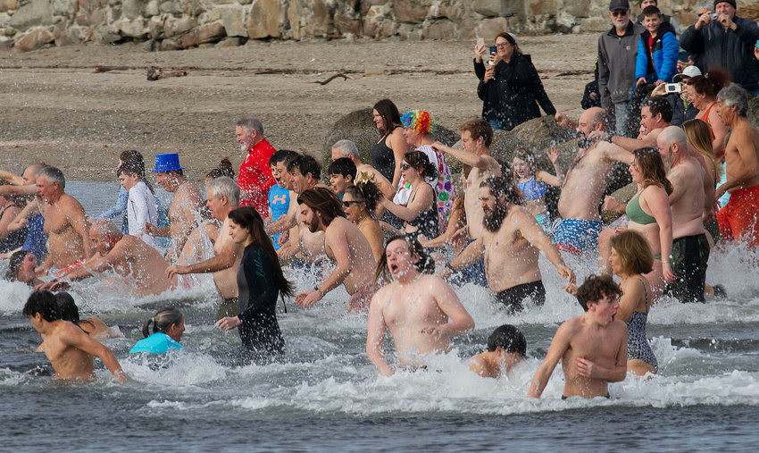A mass of revelers runs for the water at noon Sunday.