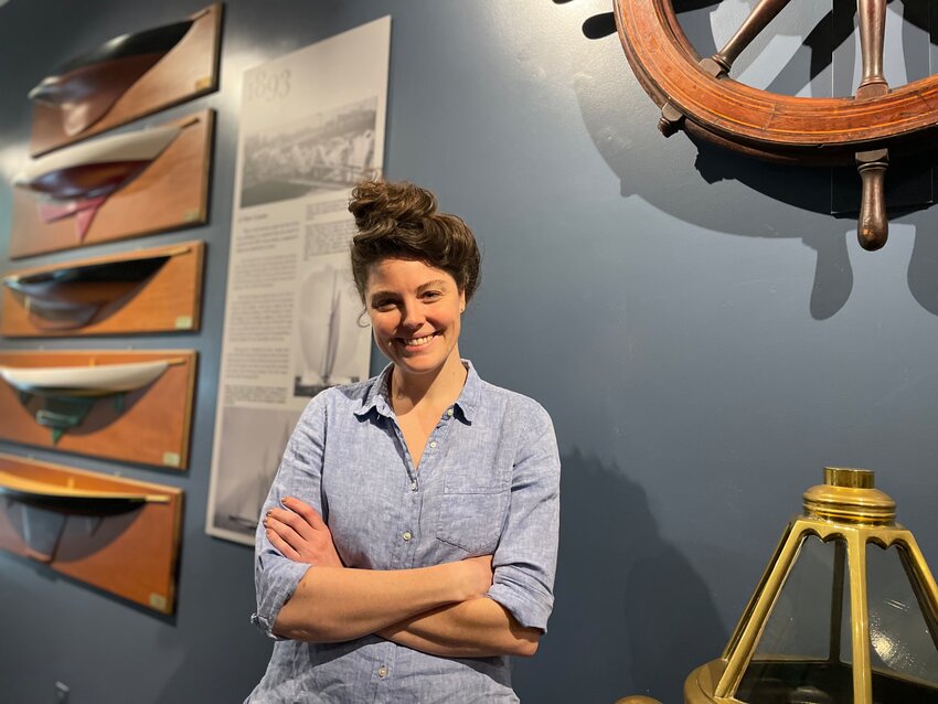Evelyn Ansel, Curator of the Herreshoff Marine Museum, at the center of the Museum&rsquo;s new permanent exhibit. To her right are some of the models carved by George I. &ldquo;Sonny&rdquo; Hodgdon, a fourth-generation builder of wooden boats. Visible on her left are the binnacle and one of the two original wheels from 1903 Cup Defender Reliance.