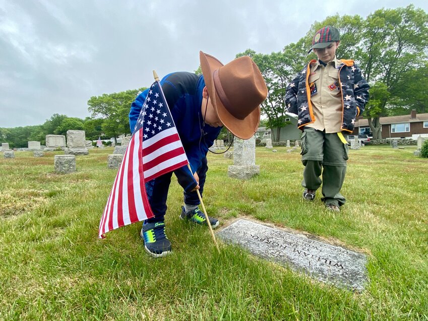 Scout Noah Laverda places a flag on the grave of a World War I veteran, while Jackson Greenwood looks on.