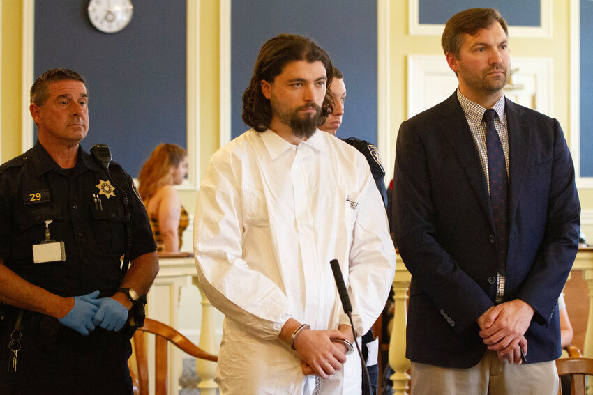 A handcuffed Jacob Morrill (center), 24, of Portsmouth, appears at his arraignment late Tuesday morning in 2nd Division District Court in Newport. He was charged with first-degree murder in the killing of his landlord, Xue Feng Wu, and ordered held without bail.