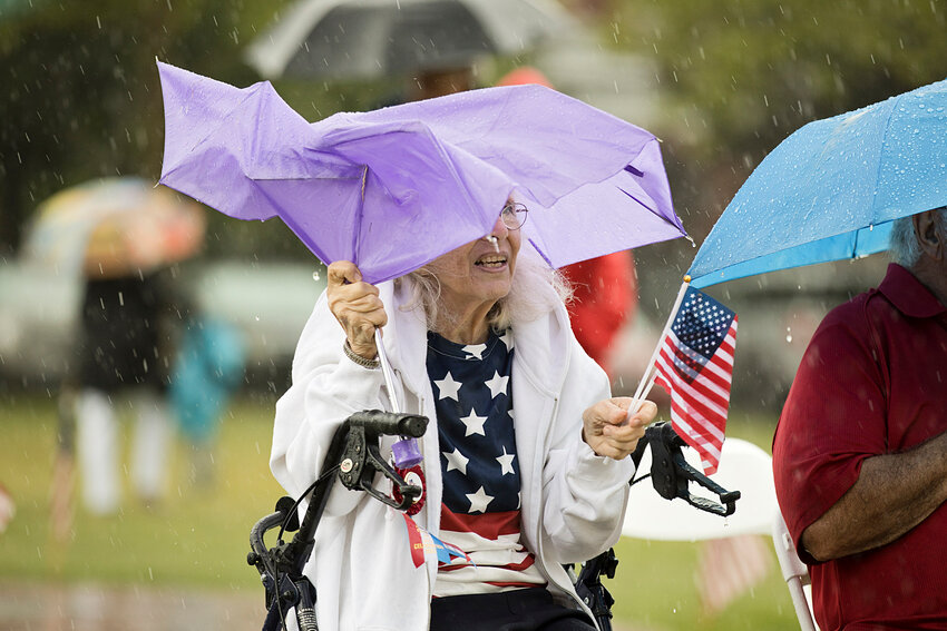 Diane Davis waves a flag while hiding under a wind-ravaged umbrella.
