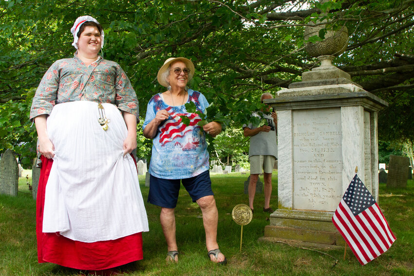 Jackie Coughlin portraying Marianne Molineux, wife of William Molineaux, a leader of the North End Caucus who was at the Boston Tea Party, and Judy Fardig of Warren take a picture with the new pin in front of the grave stone of Nicholas Campbell, an American revolutionary who was at the Boston Tea Party.