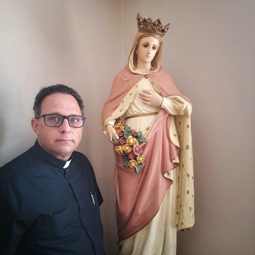 The Rev. Vander S. Martins poses alongside the statue of St. Elizabeth, who will finally have her own feast day next month.