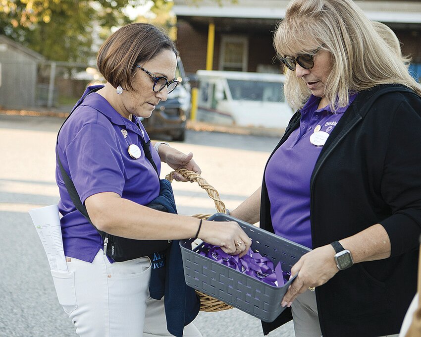 Maria Ursini (left) and Ann Marie Roy of the Warren Prevention Coalition, distribute candles and purple ribbons during this year's candlelight vigil to honor those lost to substance use disorder.