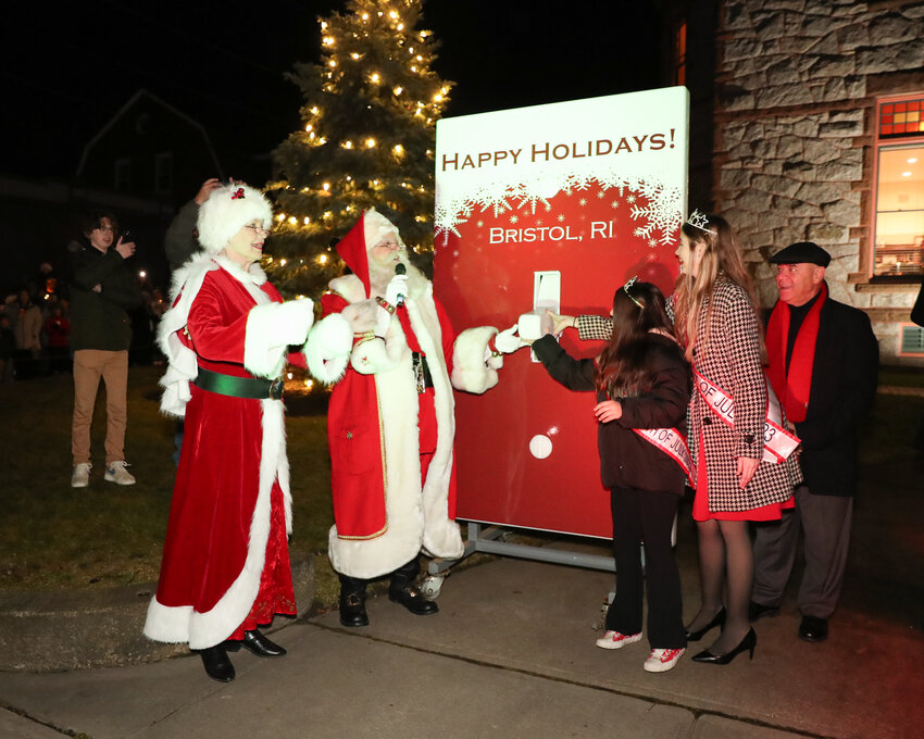 Santa and Mrs. Claus, assisted by Little Miss Fourth of July Charlotte Loftus and Miss Fourth of July Casey Little, flip the switch, while Town Councilor Tony Teixeira looks on.