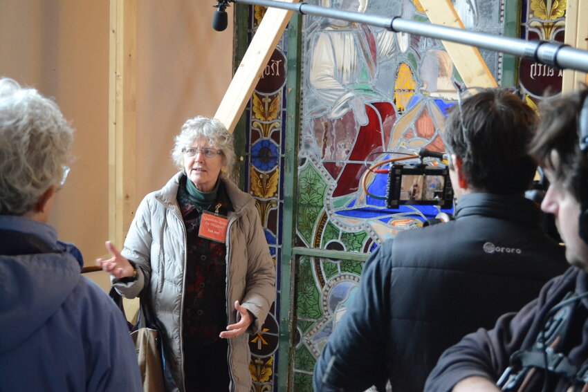Dr. Virginia Raguin talks in front of the stained glass window depicting Jesus and women Biblical figures with Black skin tones, as a documentary crew films for an upcoming feature on the window and it&rsquo;s journey to a Memphis museum.